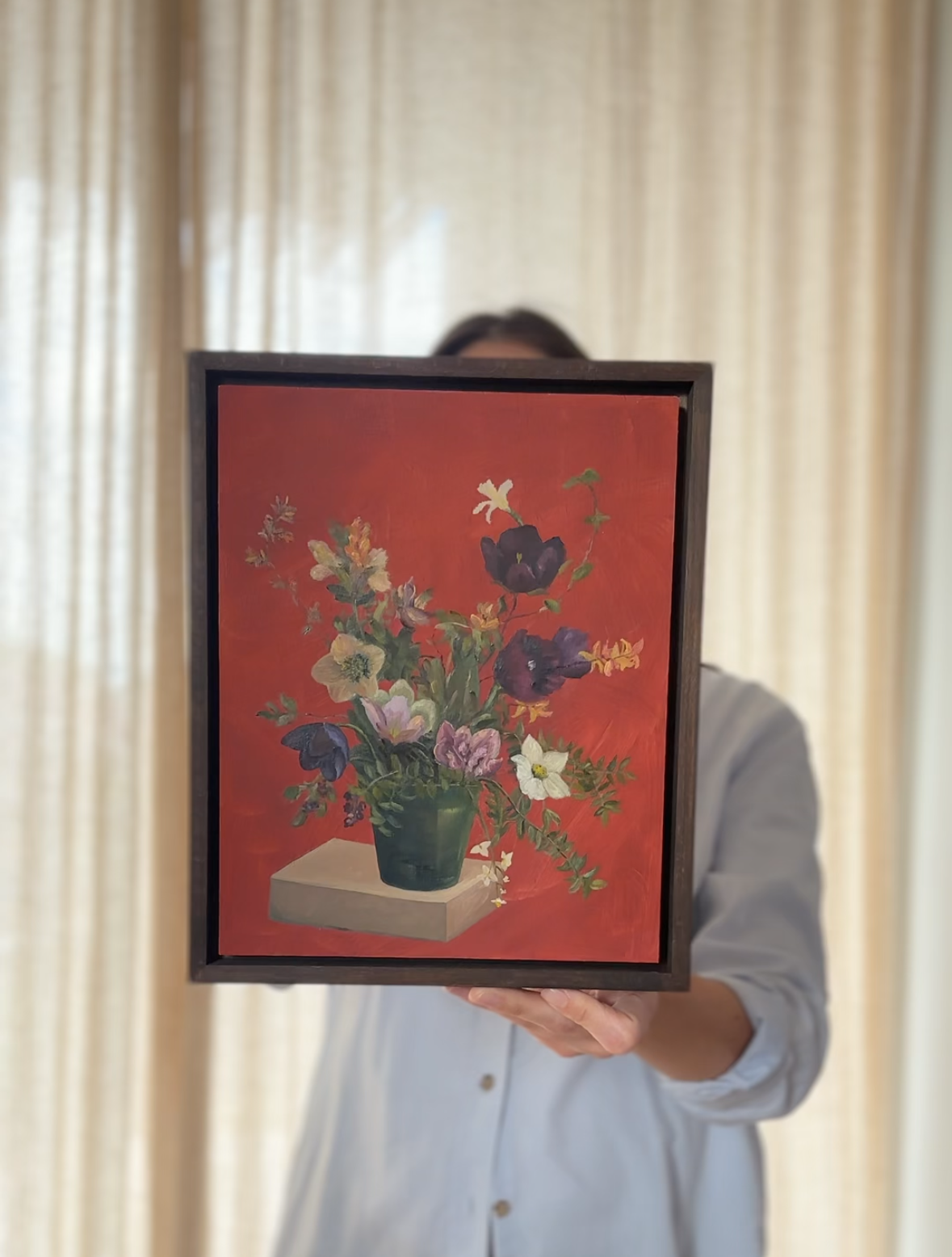 Person holding a framed painting of flowers against a red background