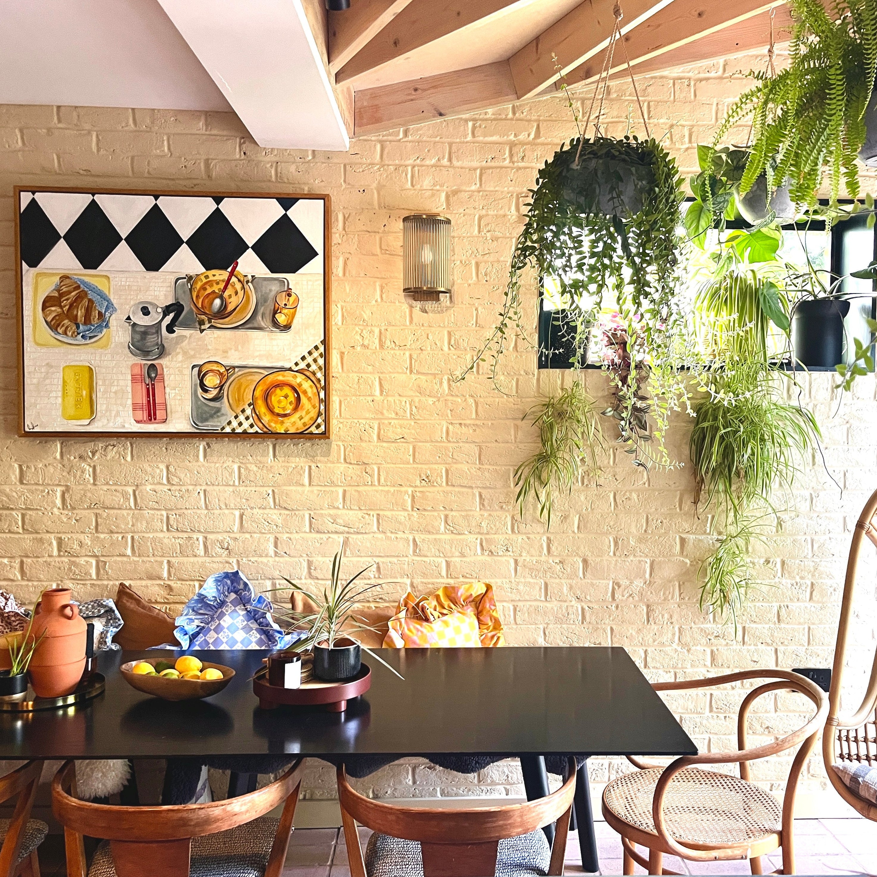 Dining area with a black table, wooden chairs, and a decorative Emma Gurner wall painting depicting a breakfast scene. 