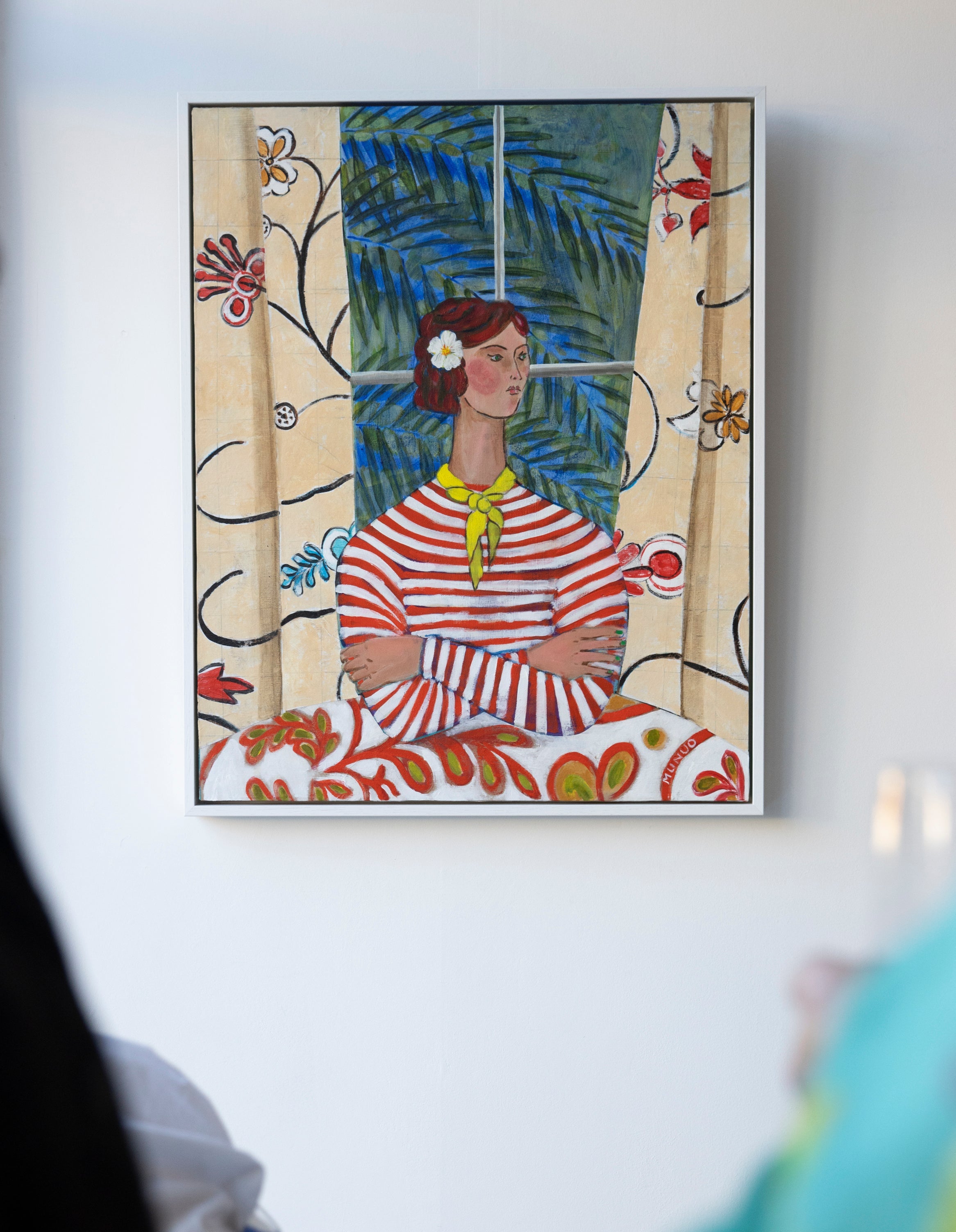 Framed artwork of a woman in a striped dress with floral and abstract elements on a white wall.