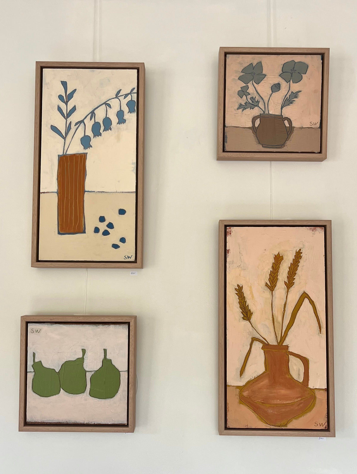 Series of four still life paintings on a wall in muted tones