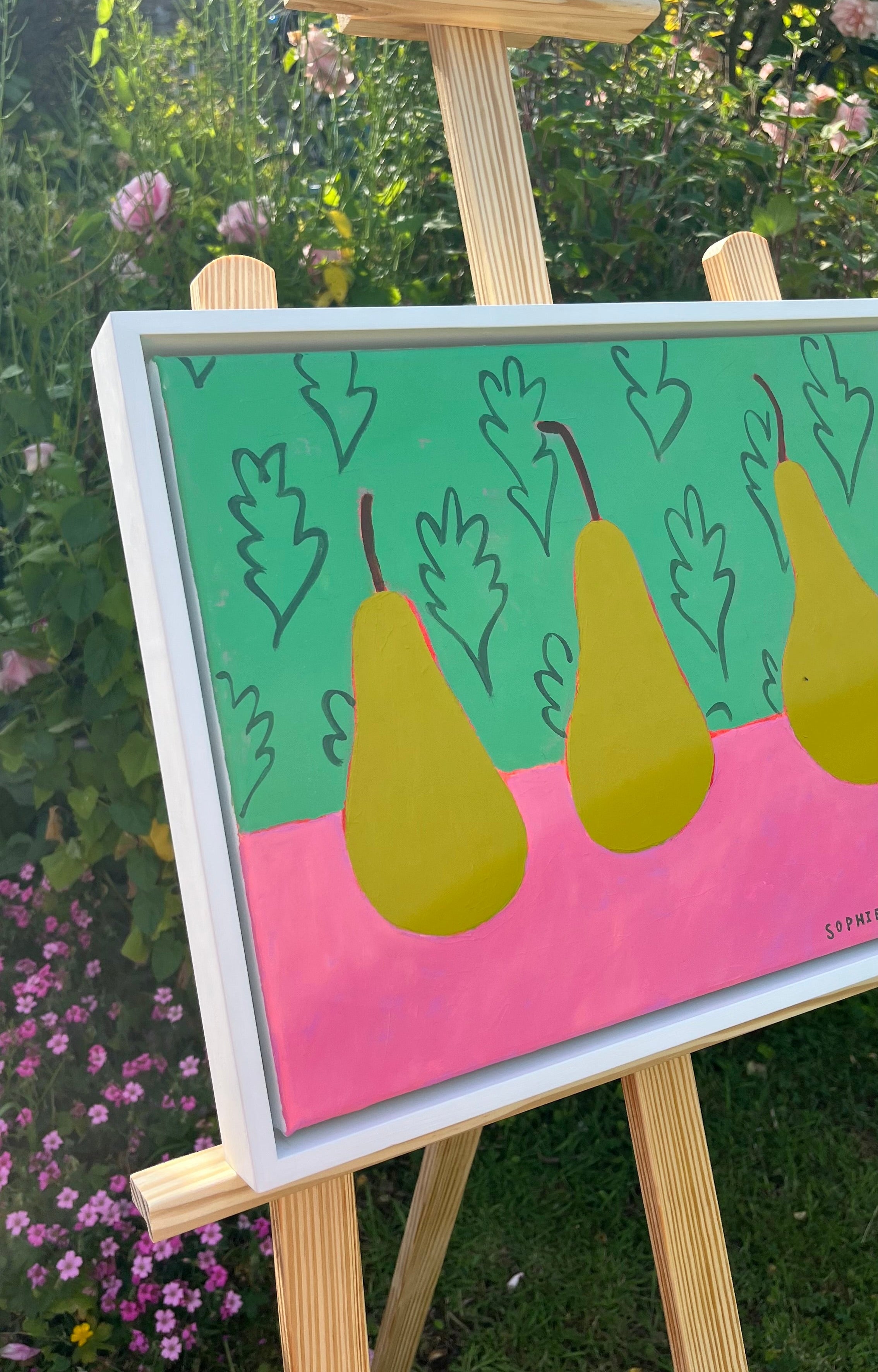 Painting of pears on a pink surface with a green background, displayed on an easel outdoors.