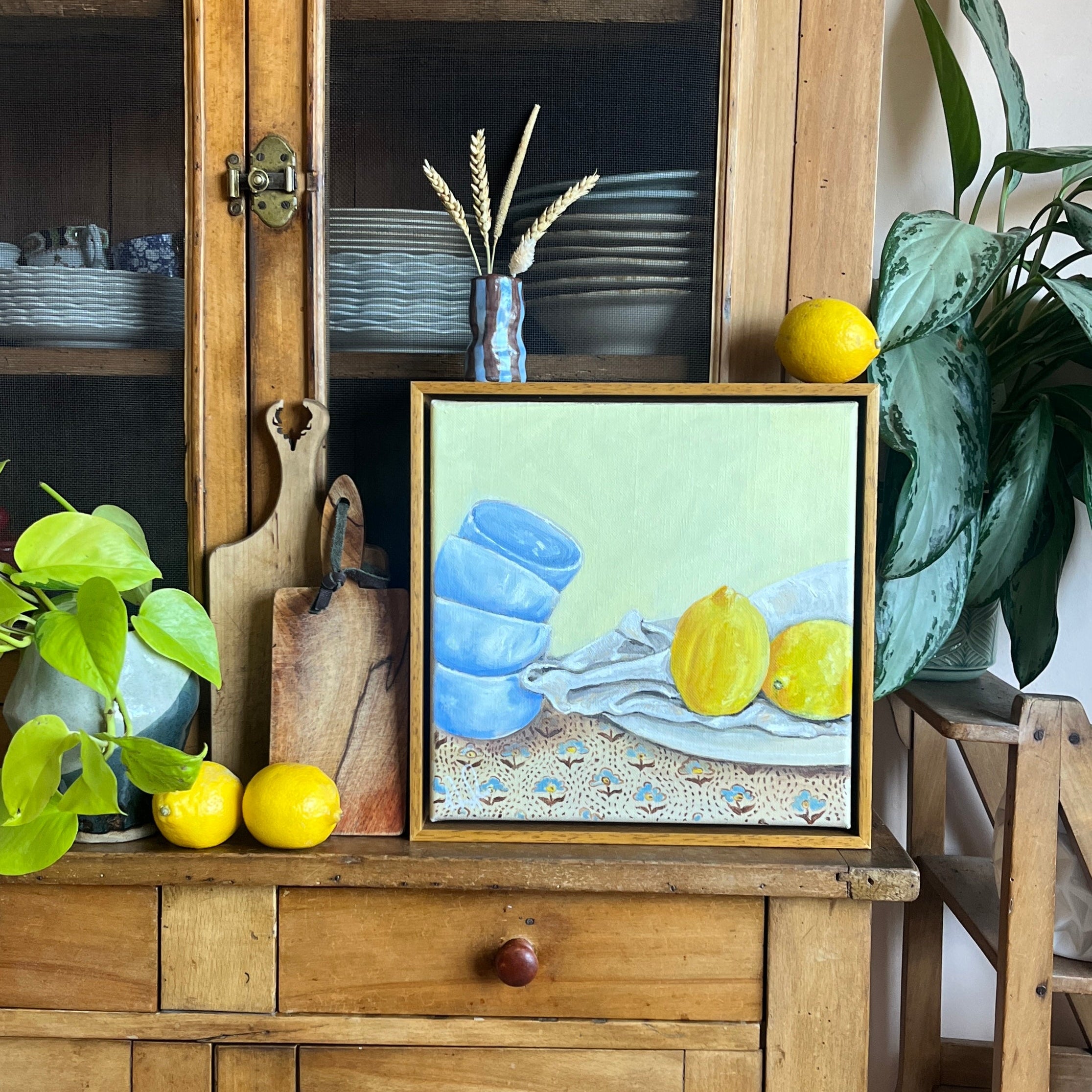 Original oil painting Stacked – With Lemons by Emma Gurner, showing stacked teacups and bright lemons in a playful naïve style, framed in an oak tray frame