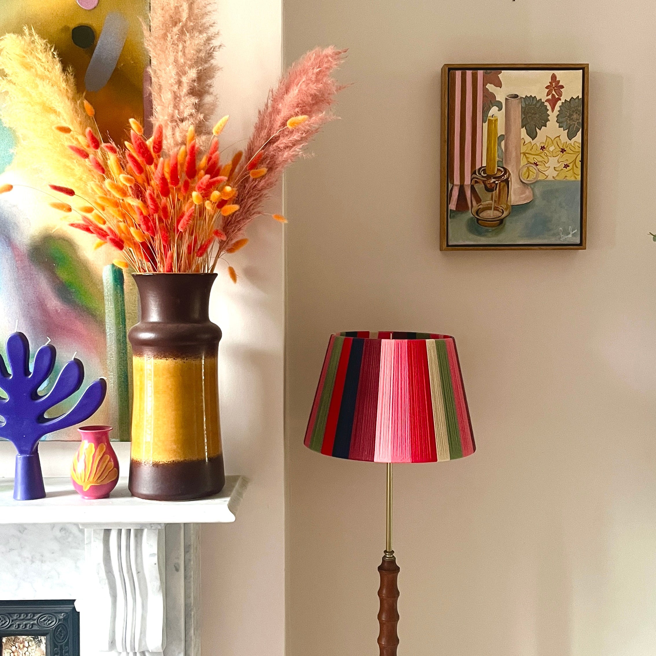 Colorful lampshade next to a shelf with decorative vases and an Emma Gurner painting on a wall.