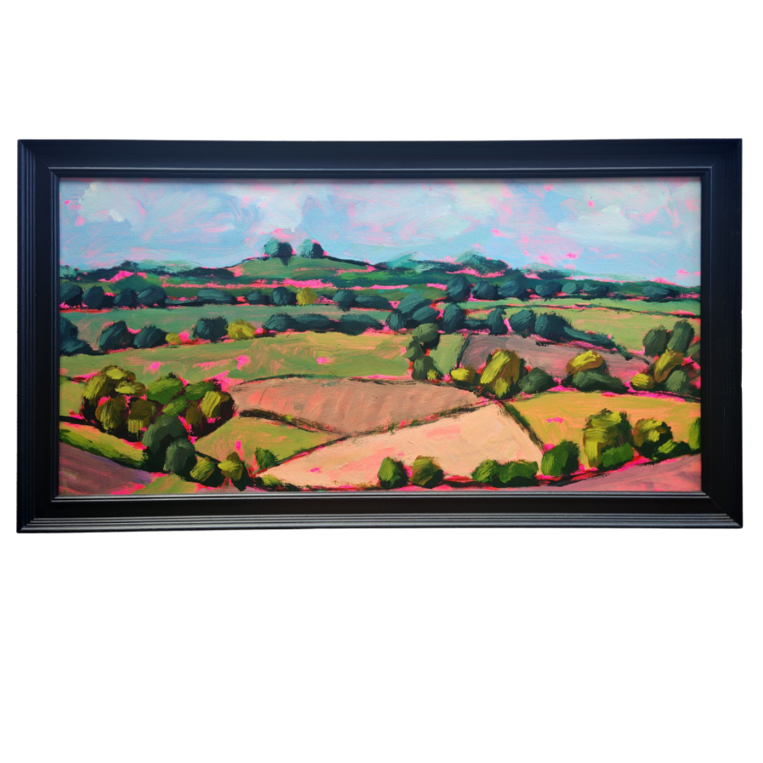 A framed landscape painting featuring rolling green hills, trees, and fields under a soft pink and blue sky, enclosed in a black frame against a white background.