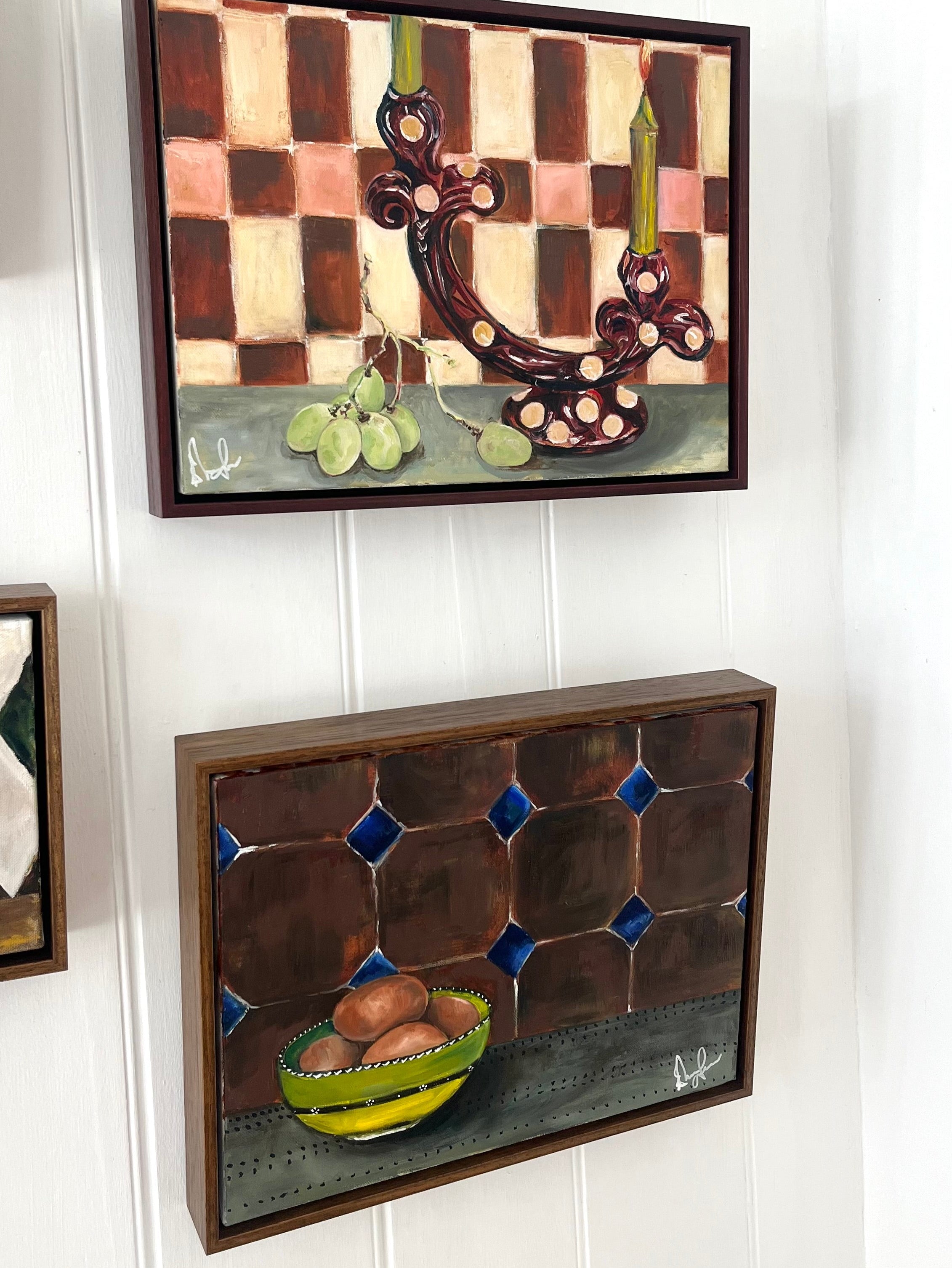Two framed artworks on a white paneled wall.