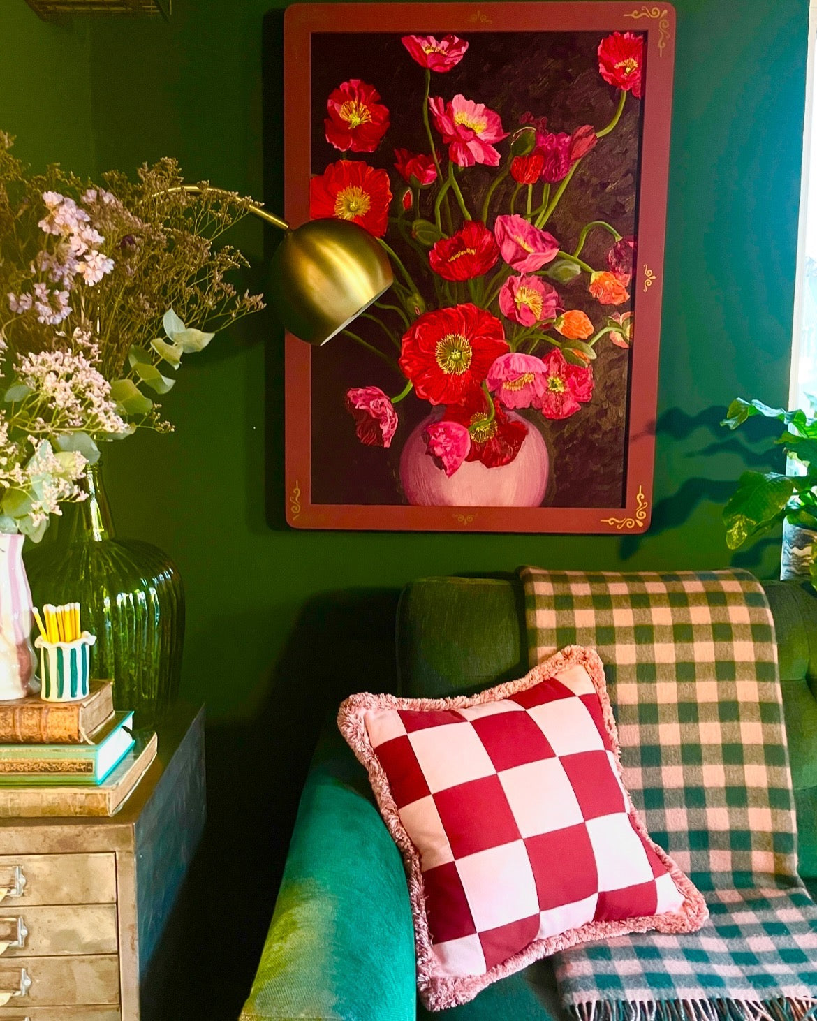 Decorative room interior with a painting of flowers, checkered pillow, and green wall.
